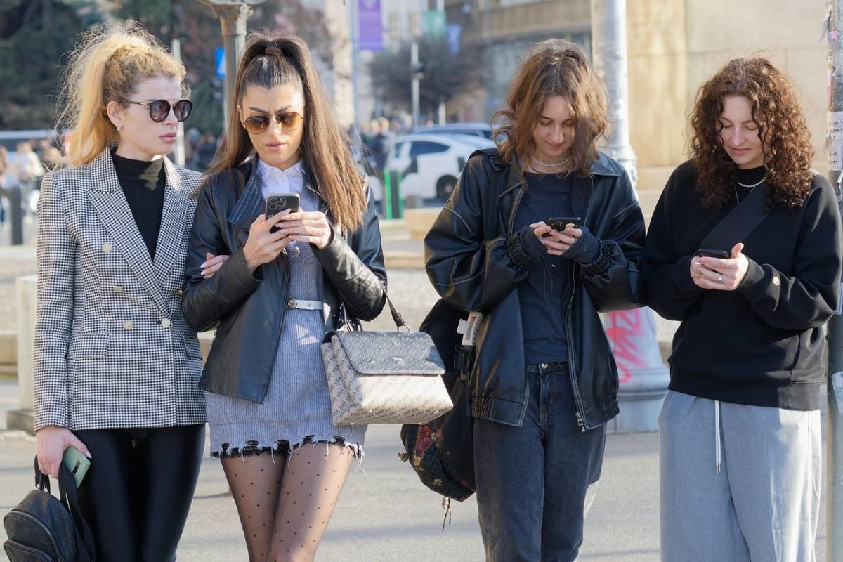 A group of young people walking on the street while distracted by their smartphones, representing digital addiction before a 24-hour digital detox.