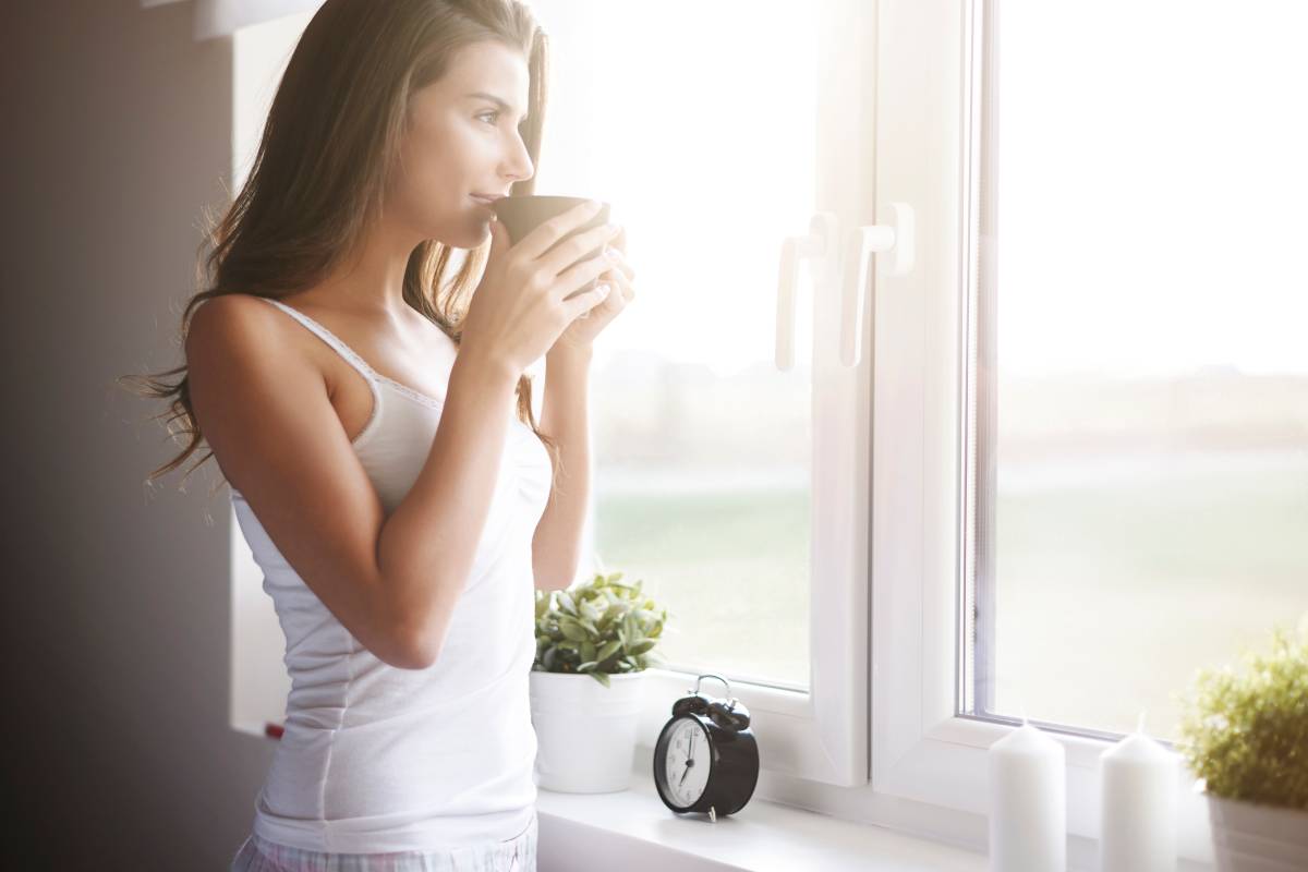 A happy woman enjoying her morning coffee by a bright window, feeling refreshed after completing a successful 24-hour digital detox.